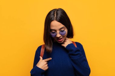 İspanyol kadın neşeyle ve gelişigüzel gülümsüyor, aşağıya bakıyor ve göğsüne işaret ediyor