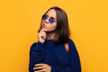 Hispanik kadın düşünüyor, şüpheci ve şaşkın hissediyor, farklı seçeneklerle, hangi kararı vereceğini merak ediyor.