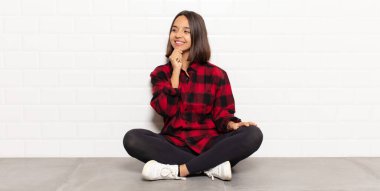 İspanyol kadın mutlu, kendinden emin bir ifadeyle gülümsüyor, çenesinde elleri, merak ediyor ve yan tarafa bakıyor.