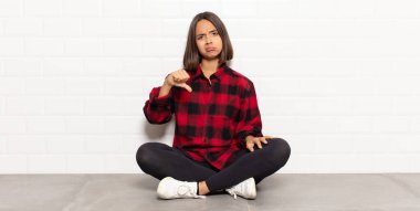 Hispanik kadın kızgın, sinirli, hayal kırıklığına uğramış ya da hoşnutsuz, ciddi bir bakışla başparmaklarını göstermiyor.