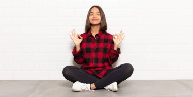 Hispanik kadın odaklanmış ve meditasyon yapıyor, tatmin olmuş ve rahatlamış hissediyor, düşünüyor ya da bir seçim yapıyor.