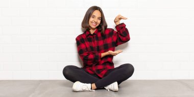 İspanyol kadın gülümsüyor, mutlu, pozitif ve tatmin olmuş hissediyor, fotokopi alanında nesne veya konsept tutuyor veya gösteriyor