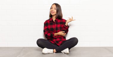 Hispanik kadın gururla ve kendinden emin bir şekilde gülümsüyor, mutlu ve tatmin olmuş hissediyor ve fotokopi alanında bir konsept gösteriyor.