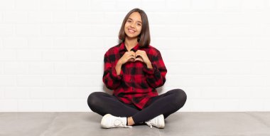 İspanyol kadın gülümsüyor ve mutlu, sevimli, romantik ve aşık, iki eliyle kalbi şekillendiriyor.