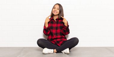 İspanyol kadın kendine güvenerek gülümsüyor. Kendi gülüşünü gösteriyor. Olumlu, rahat, tatmin olmuş tavır.