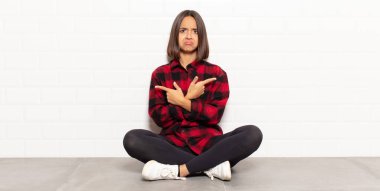 İspanyol kadın şaşkın ve şaşkın görünüyor, güvensiz ve şüpheyle zıt yönleri işaret ediyor.