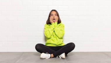 İspanyol kadın şok olmuş ve korkmuş hissediyor, ağzı açık ve elleri yanaklarında korkmuş görünüyor.