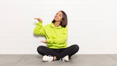 İspanyol bir kadın, iki eli yanda olan bir objeyi tutuyor fotokopi alanında, bir nesneyi gösteriyor, sunuyor ya da reklamını yapıyor.