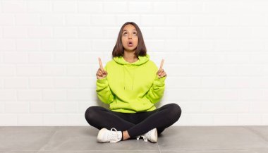 Hispanik kadın şaşkınlık içinde ve ağzı açık. Şok olmuş ve şaşırmış bir bakışla yukarı bakıyor.