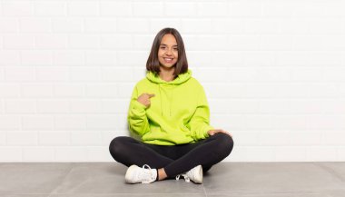 İspanyol kadın gururlu, kendinden emin ve mutlu görünüyor, gülümsüyor ve kendini işaret ediyor ya da bir numara işareti yapıyor.