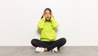 İspanyol kadın hoş olmayan bir şekilde şok olmuş, korkmuş ya da endişeli görünüyor, ağzı sonuna kadar açık ve iki kulağını da elleriyle kapatıyor.