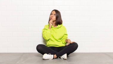 Hispanik kadın düşünüyor, şüpheci ve şaşkın hissediyor, farklı seçeneklerle, hangi kararı vereceğini merak ediyor.