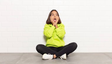 Hispanik kadın mutlu, heyecanlı ve şaşırmış hissediyor, iki eli yüzü yana bakıyor