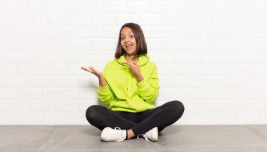 İspanyol kadın neşeli bir şekilde gülümsüyor ve bir objeyi gösteren veya reklamını yapan avuç içindeki fotokopi alanını işaret ediyor.