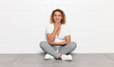 Orta yaşlı kadın mutlu görünüyor ve gülümsüyor. Elleri çenesinde, merak ediyor ya da soru soruyor. Seçenekleri karşılaştırıyor.