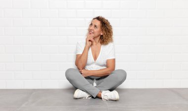 Orta yaşlı bir kadın mutlu bir şekilde gülümsüyor ve hayal kuruyor ya da şüphe ediyor.