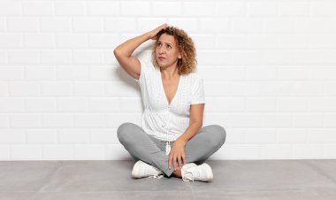 Orta yaşlı kadın şaşkın ve şaşkın hissediyor, kafasını kaşıyor ve yan tarafa bakıyor.