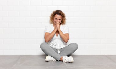 Orta yaşlı bir kadın mutlu, neşeli, şanslı ve şaşkın görünüyor. İki eliyle ağzını kapatıyor.