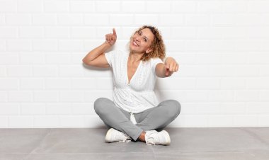 Orta yaşlı bir kadın mutlu ve kendinden emin, kamerayı iki eliyle gösteriyor ve gülüyor, seni seçiyor.