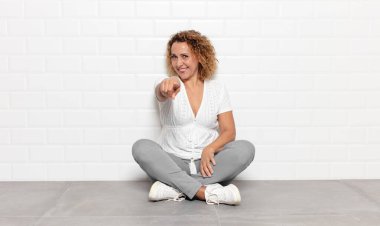 Orta yaşlı bir kadın kameraya bakıyor, kendinden emin, arkadaş canlısı bir gülümsemeyle, seni seçiyor.