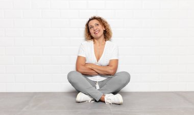 Orta yaşlı bir kadın mutlu, gururlu ve umutlu, merak ediyor ya da düşünüyor, çapraz kollarla fotokopi çekmeyi bekliyor.