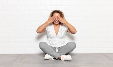 Orta yaşlı bir kadın gülümsüyor ve mutlu hissediyor, iki eliyle gözlerini kapatıyor ve inanılmaz bir sürpriz bekliyor.