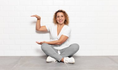 Orta yaşlı kadın gülümsüyor, mutlu, pozitif ve tatmin olmuş hissediyor, fotokopi alanında nesne veya konsept tutuyor veya gösteriyor