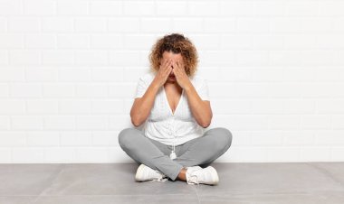 Orta yaşlı bir kadın üzgün, hayal kırıklığına uğramış, gergin ve bunalımda, yüzünü iki eliyle kapatıyor, ağlıyor.