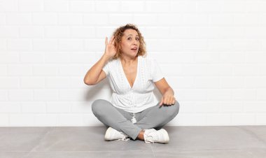 Orta yaşlı kadın gülümsüyor, tuhaf bir şekilde yan tarafa bakıyor, dedikoduları dinlemeye ya da bir sırrı duymaya çalışıyor.