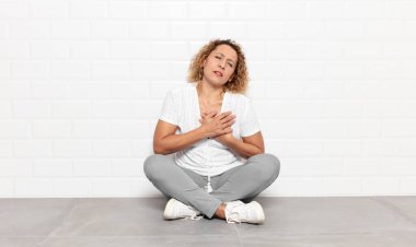 Orta yaşlı bir kadın üzgün, yaralı ve kalbi kırık görünüyor, iki elini de kalbe yakın tutuyor, ağlıyor ve bunalımda.