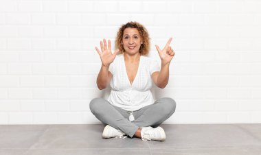 Orta yaşlı bir kadın gülümsüyor ve dost canlısı görünüyor, 7 ya da 7 numarayı gösteriyor, eli önde, geriye doğru sayıyor.