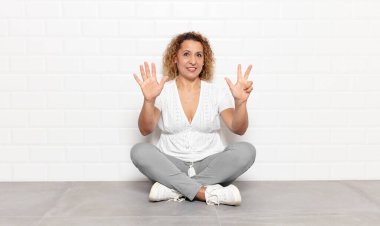 Orta yaşlı bir kadın gülümsüyor ve arkadaş canlısı görünüyor, 8 ya da 8 numarayı gösteriyor, elleri önde, geriye doğru sayıyor.