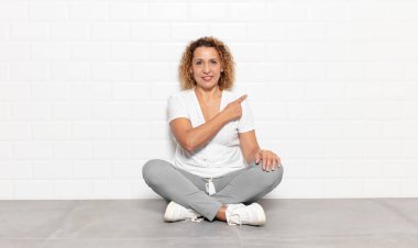 Orta yaşlı kadın neşeli bir şekilde gülümsüyor, mutlu hissediyor ve yan ve yukarı doğru işaret ediyor, fotokopi uzayındaki nesneleri gösteriyor.