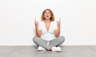 Orta yaşlı bir kadın şaşırmış, şaşırmış ve ağzı açık bir şekilde iki elini de havaya kaldırıp boşluğu dolduruyor.