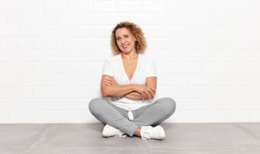 Orta yaşlı bir kadın kollarını kavuşturup mutlu bir şekilde gülüyor, rahat, pozitif ve tatmin edici bir pozla.