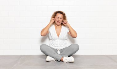 Orta yaşlı bir kadın sinirli, stresli ve sinirli görünüyor, iki kulağını da sağır edici bir ses, ses ya da yüksek sesle kapatıyor.