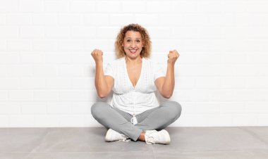 Orta yaşlı bir kadın mutlu, şaşırmış ve gururlu hissediyor, bağırıyor ve başarıyı büyük bir gülümsemeyle kutluyor.