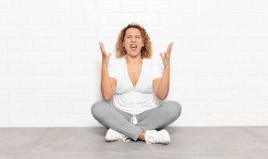 Orta yaşlı bir kadın öfkeyle bağırıyor, stresli hissediyor ve ellerini havaya kaldırıp neden ben diye bağırıyor.