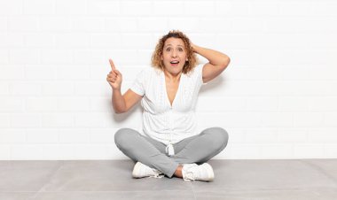 Orta yaşlı bir kadın gülüyor, mutlu, pozitif ve şaşırmış görünüyor, yanal fotokopi alanını işaret eden harika bir fikrin farkına varıyor.