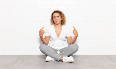 Kötü tavırlı orta yaşlı bir kadın gururlu ve agresif görünüyor, yukarıyı gösteriyor ya da elleriyle alay işareti yapıyor.