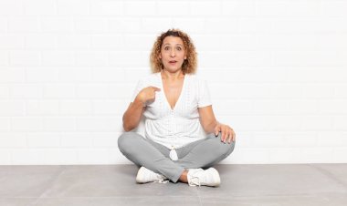 Orta yaşlı kadın şok olmuş ve şaşırmış görünüyor ağzı açık, kendini işaret ediyor.