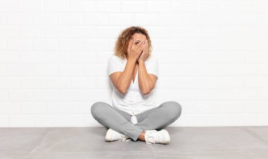 Orta yaşlı bir kadın korkmuş ya da utanmış hisseder. Gözleri yarı kapalı, yarı çıplak bir şekilde dikizler ya da gözetler.