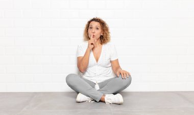 Orta yaşlı bir kadın sessizlik ve sessizlik istiyor, parmağıyla ağzının önünde işaret ediyor, 