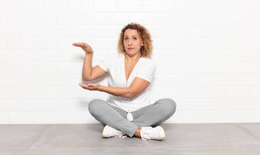 Orta yaşlı bir kadın bir objeyi iki eliyle fotokopi alanında tutuyor, bir objeyi gösteriyor, sunuyor ya da reklamını yapıyor.