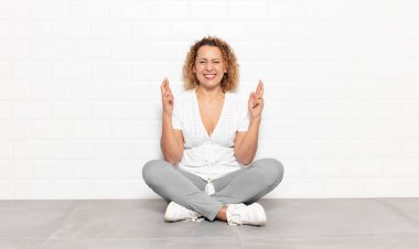 Orta yaşlı kadın gülümsüyor ve endişeyle iki parmağını çapraz yapıyor. Endişeli hissediyor, iyi şanslar diliyor ya da umut ediyor.