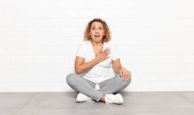 Orta yaşlı bir kadın şaşkın ve şaşırmış hissediyor, gülümsüyor, el ele tutuşuyor, o olmaktan mutlu ya da minnettarlık gösteriyor.