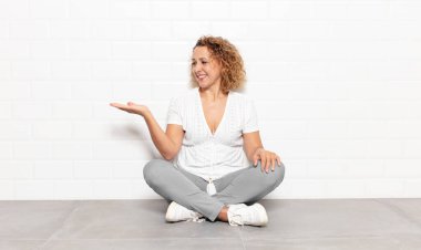 Orta yaşlı bir kadın kendini mutlu hissediyor ve gülümsüyor. Elinde tuttuğu bir nesneye ya da konsepte bakıyor.