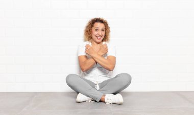 Orta yaşlı bir kadın neşeli bir şekilde gülümsüyor ve yumruklarını sıkmış, kollarını kavuşturmuş, mutlu ve pozitif hissediyor.