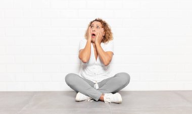 Orta yaşlı bir kadın, mutlu, heyecanlı ve şaşırmış hissediyor, iki eli yüzü yana bakıyor.