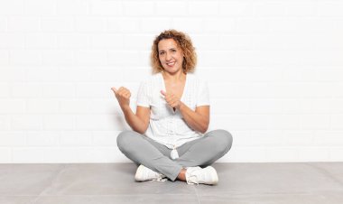 Orta yaşlı kadın neşeli bir şekilde gülümsüyor ve yan taraftaki fotokopi alanını işaret ediyor, mutlu ve tatmin olmuş hissediyor.